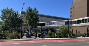 View of the Encore Terrace at RBC Place London from across the street, with people walking and trees lining the entrance on a sunny day.