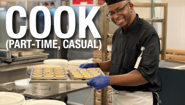 A chef in black smiles for the camera while holding a tray of hors d'oeuvres in the kitchen at RBC Place London