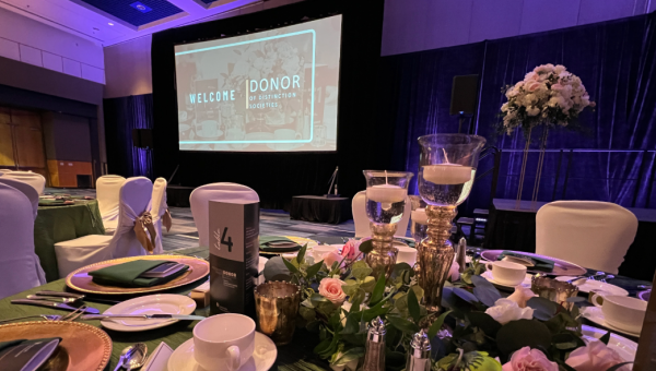 Elegant banquet table set with floral centerpieces and candles in a dimly lit ballroom featuring a large screen welcoming donors to the Donors of Distinction President's Dinner. This year's dinner will return to RBC Place London on May 13, 2026.